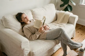 Femme se reposant paisiblement sur un canapé en lin avec un livre, illustrant l'importance du repos le week-end